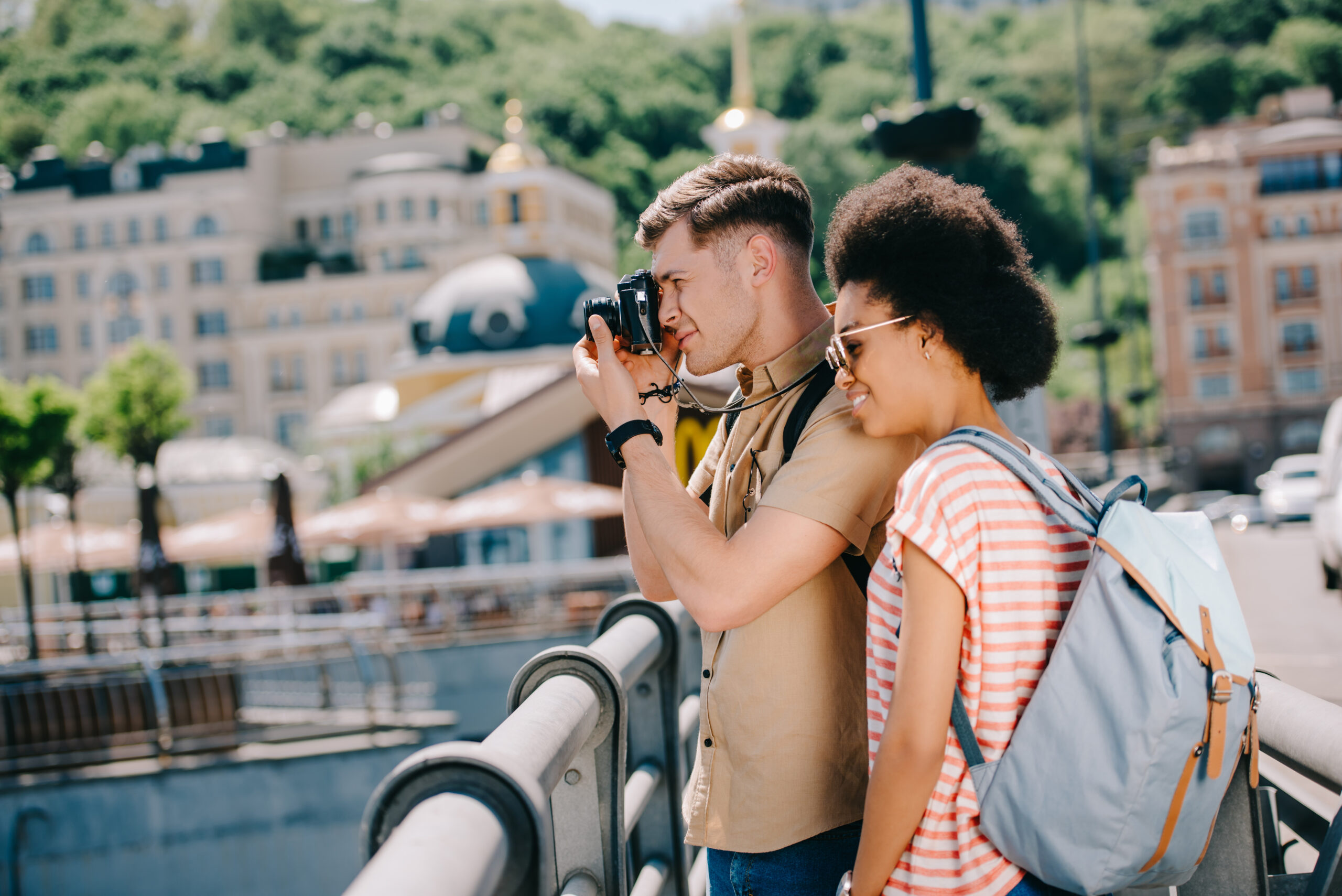 side view of male traveler taking picture on camera and african american girlfriend standing near